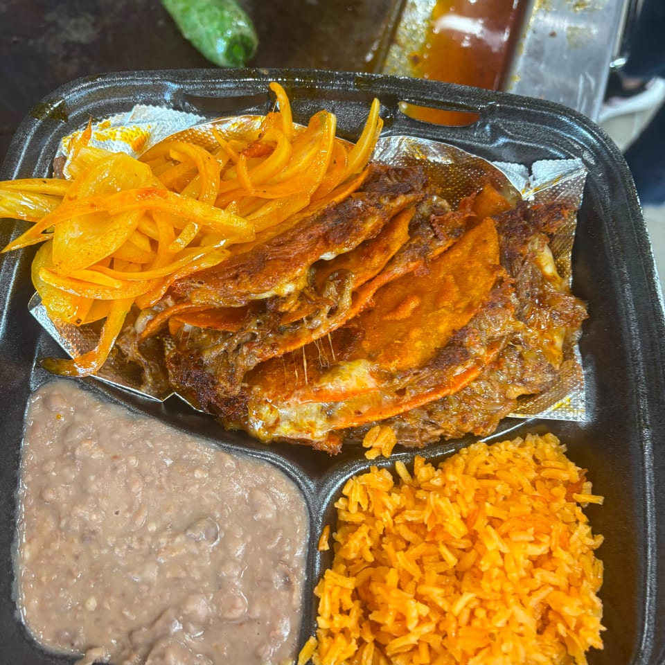 A takeout container filled with birria tacos, rice, refried beans, and pickled onions.
