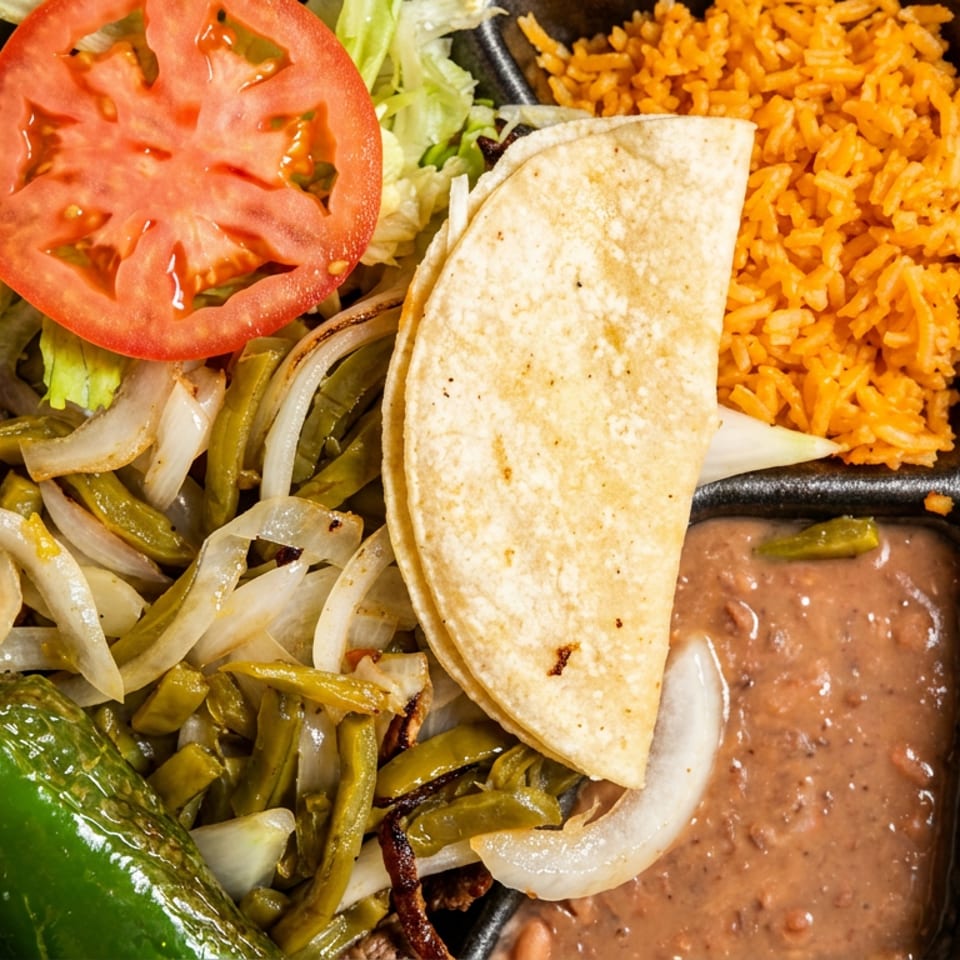 Mexican meal in a takeout container with corn tortilla, rice, beans, sautéed vegetables, tomato, and chili.