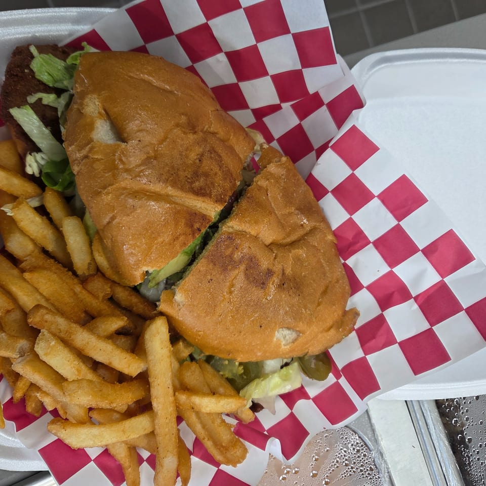 A large sandwich cut in half with lettuce and pickles, served with a side of golden fries.