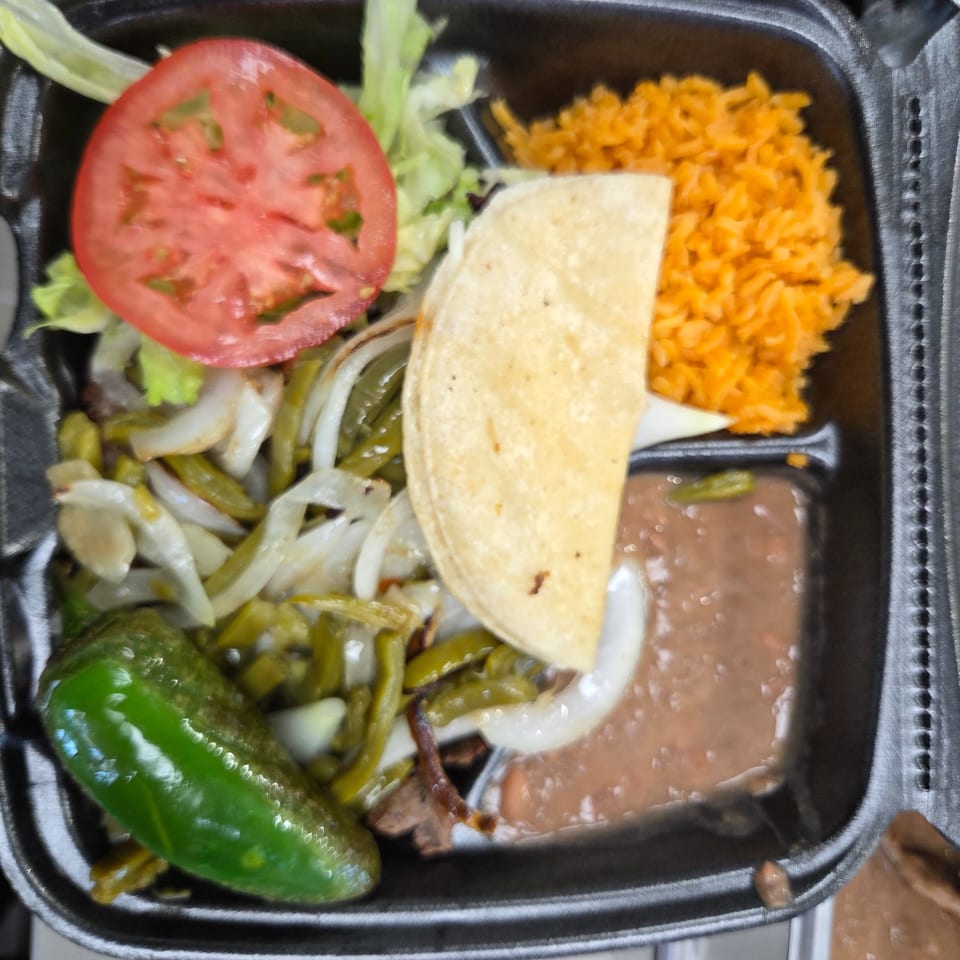 Mexican takeout meal with rice, beans, taco, grilled peppers, onions, tomato, and lettuce.
